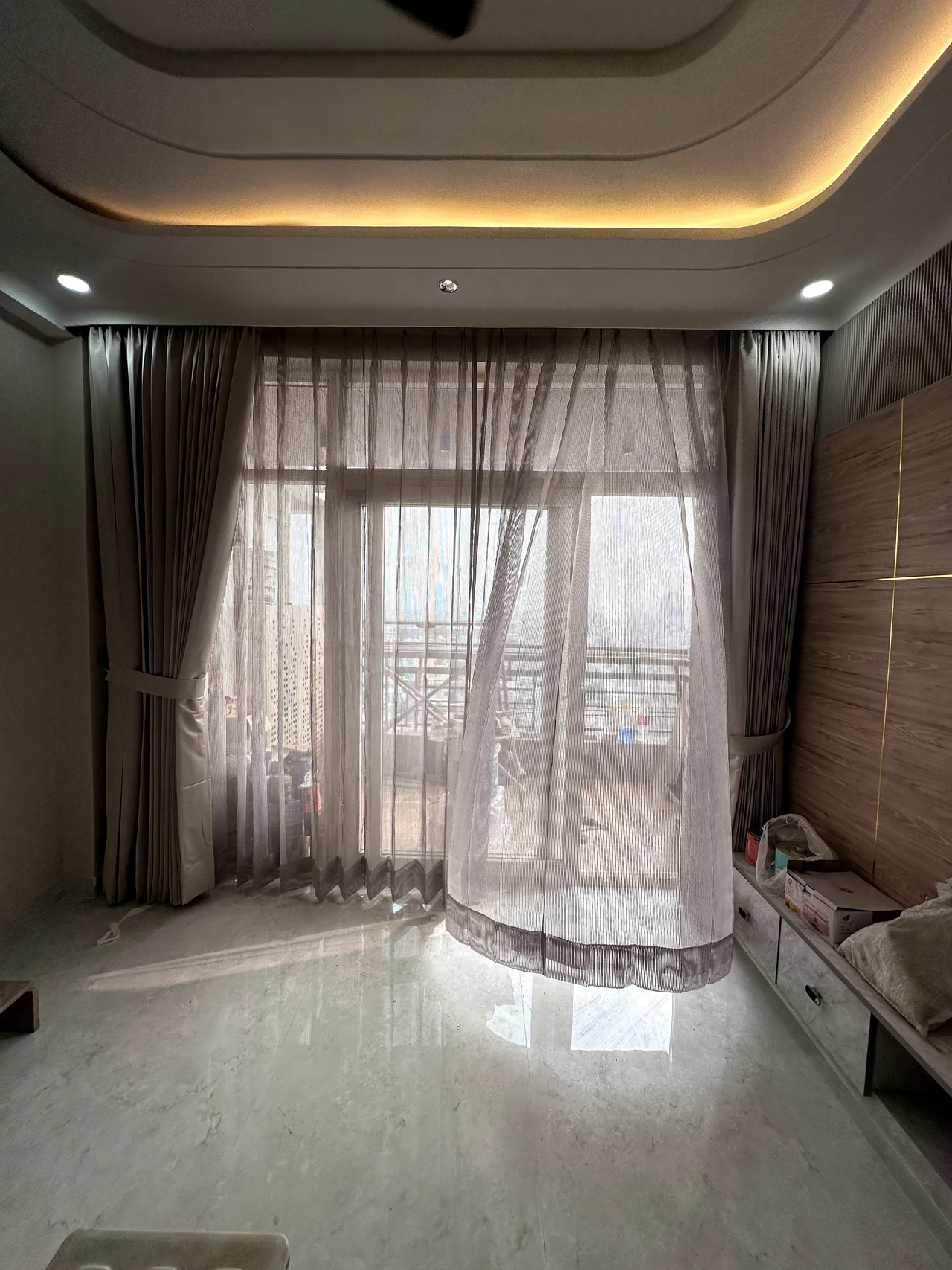 Living room and balcony framed by layered curtains and a cove-lit ceiling