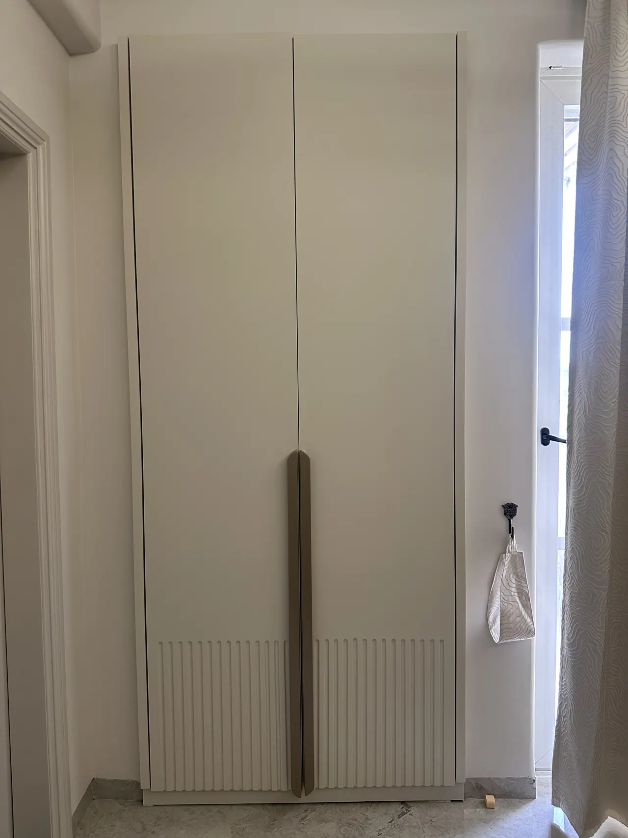 Fluted wardrobe with a long brass-tone handle and daylight